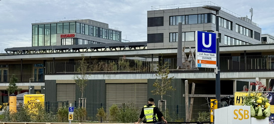 一座现代建筑的外观，右侧有一个地铁站标志，上面写着“Stadtbahnhof”，左侧有一名穿着制服的人，建筑周围有绿化。